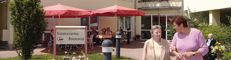 Foto vor dem Seniorenzentrum in Bräunlingen. Eingang und rote Schirme - darunter sitzt eine Gruppe von Menschen.